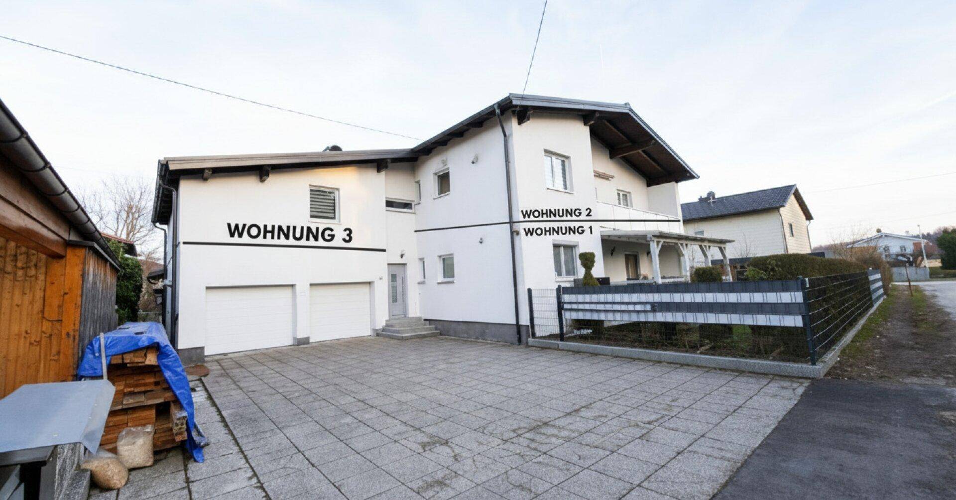 Vorderansicht des Hauses mit drei Wohneinheiten und gepflastertem Vorplatz.