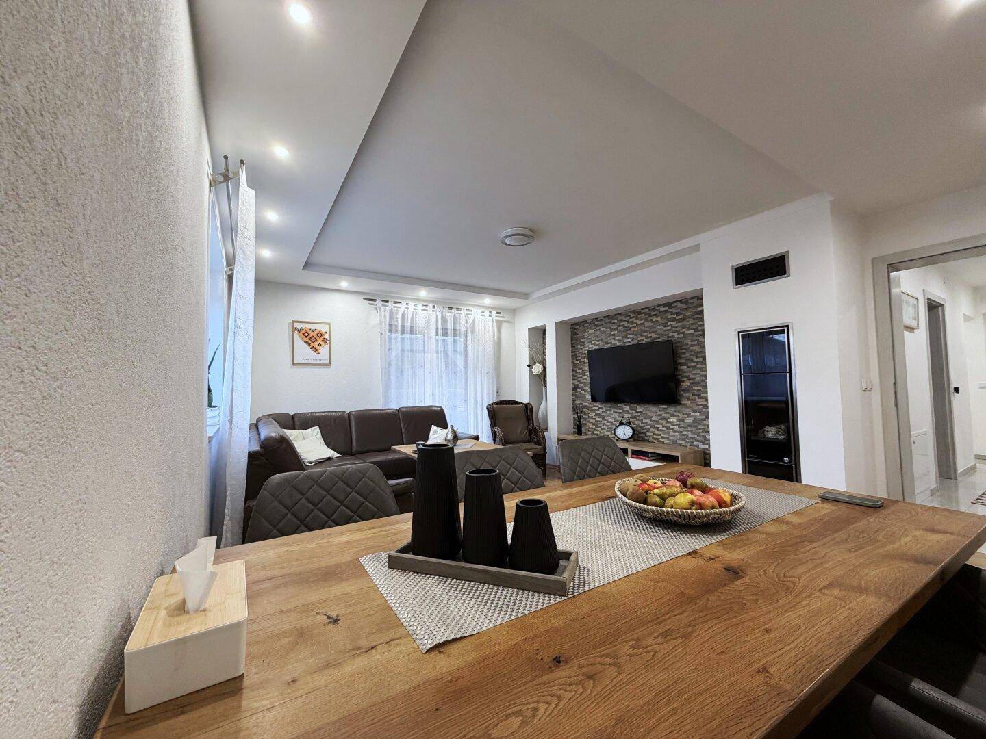 Moderner Wohn-Essbereich mit Holzboden, dunklem Sofa und dekorativer Wandgestaltung.