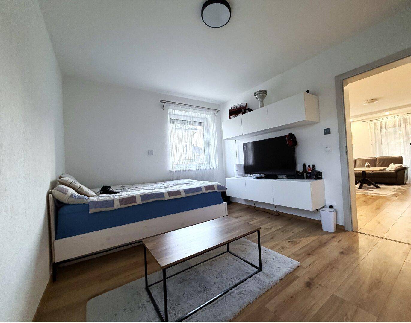 Schlafzimmer mit Holzboden, Einzelbett und Wandregal mit Fernseher.