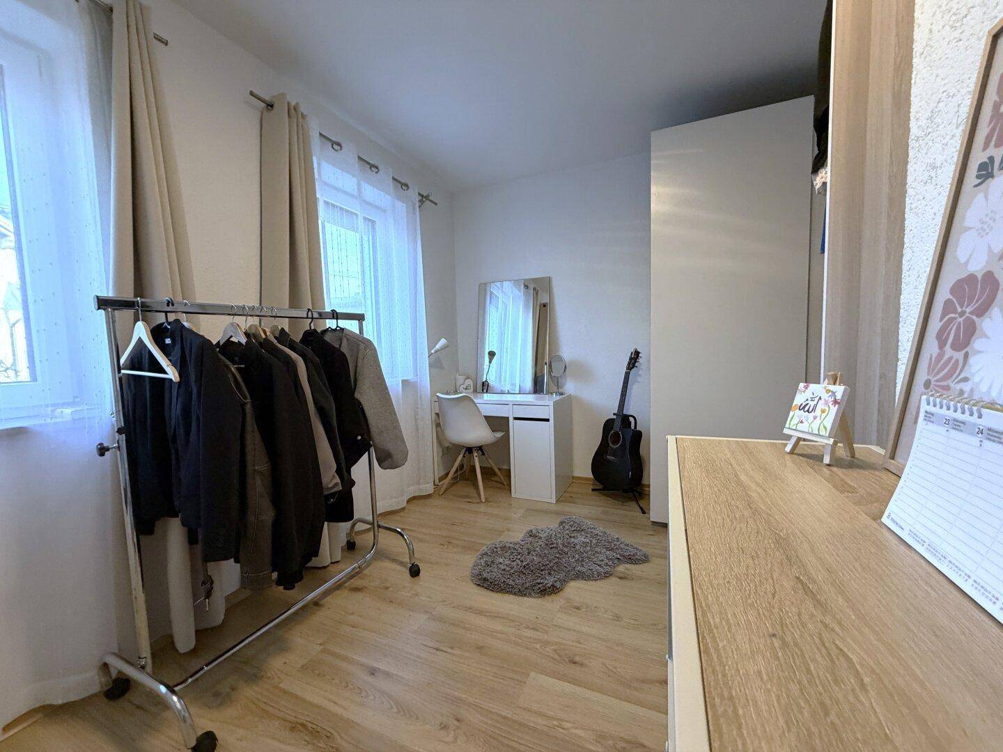 Schlafzimmer mit Holzboden, Schreibtisch und Kleiderstange, ideal für Gäste oder Kinder.