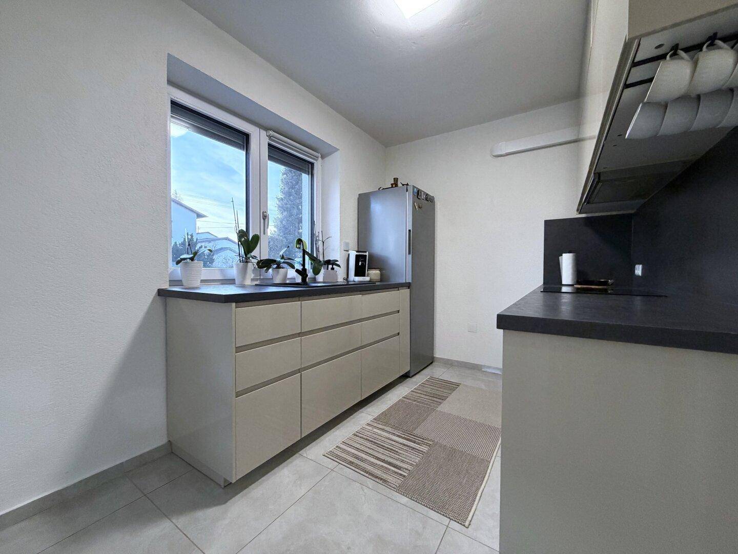 Helle Küche mit beigen Unterschränken, dunkler Arbeitsplatte und Fensterblick.