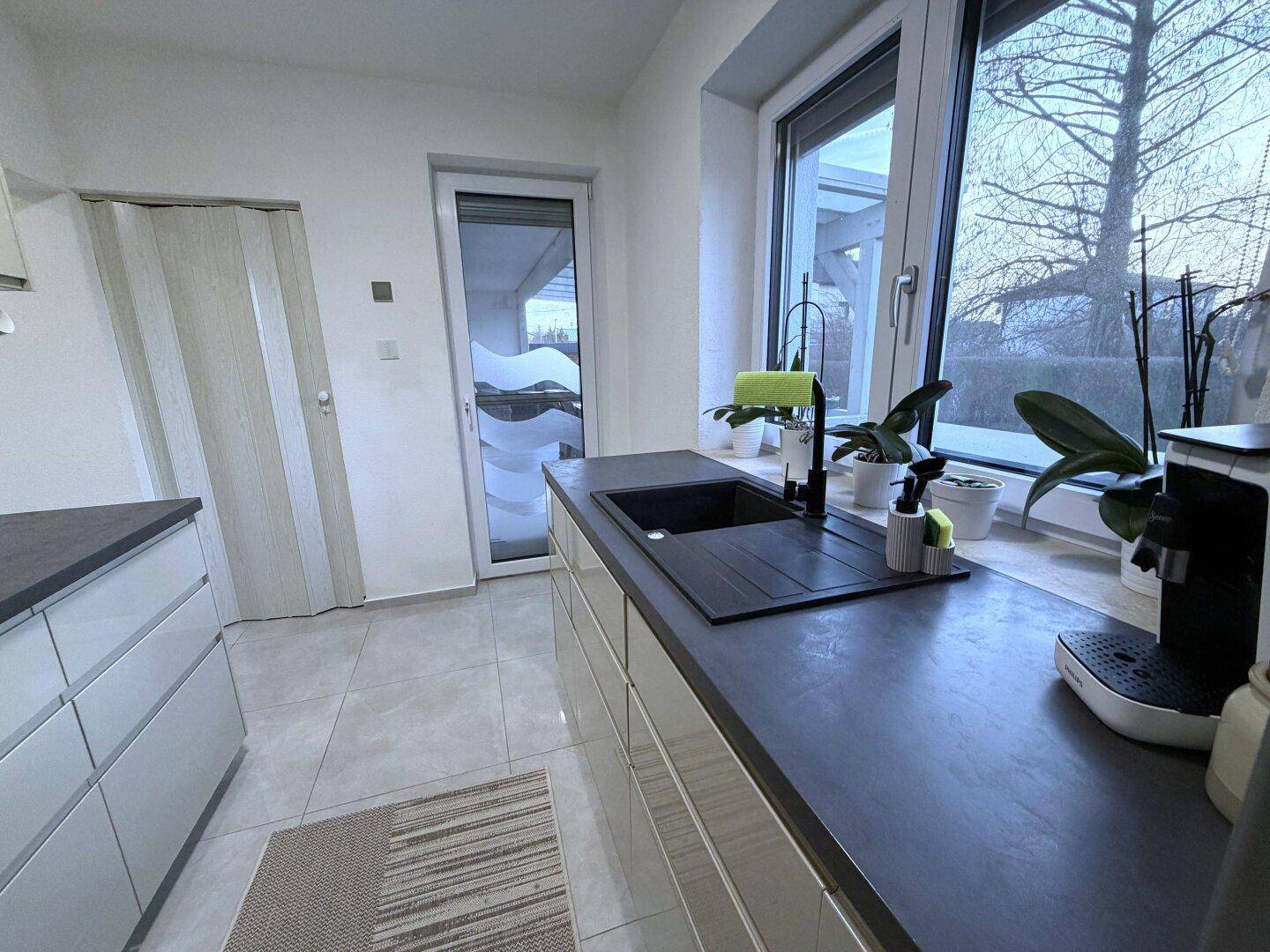 Moderne Küche mit dunkler Arbeitsplatte, Spüle und Zugang zur Terrasse.