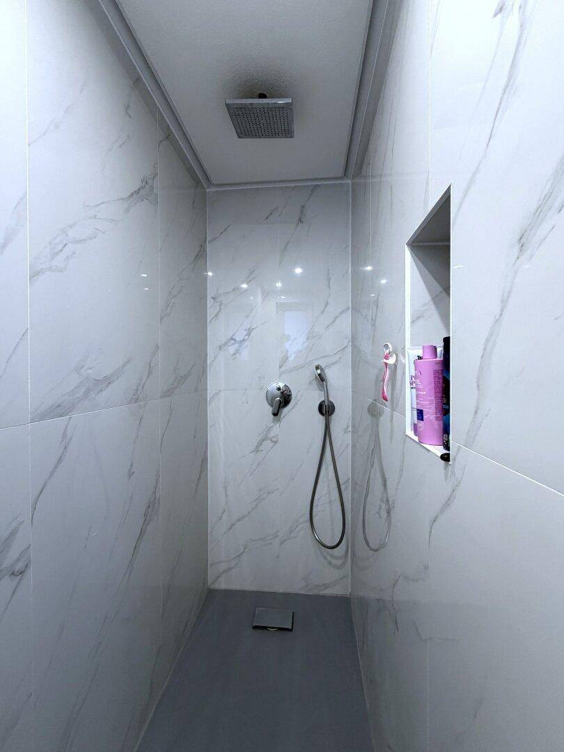 Moderne Duschkabine mit weißen Marmorfliesen und Regendusche.