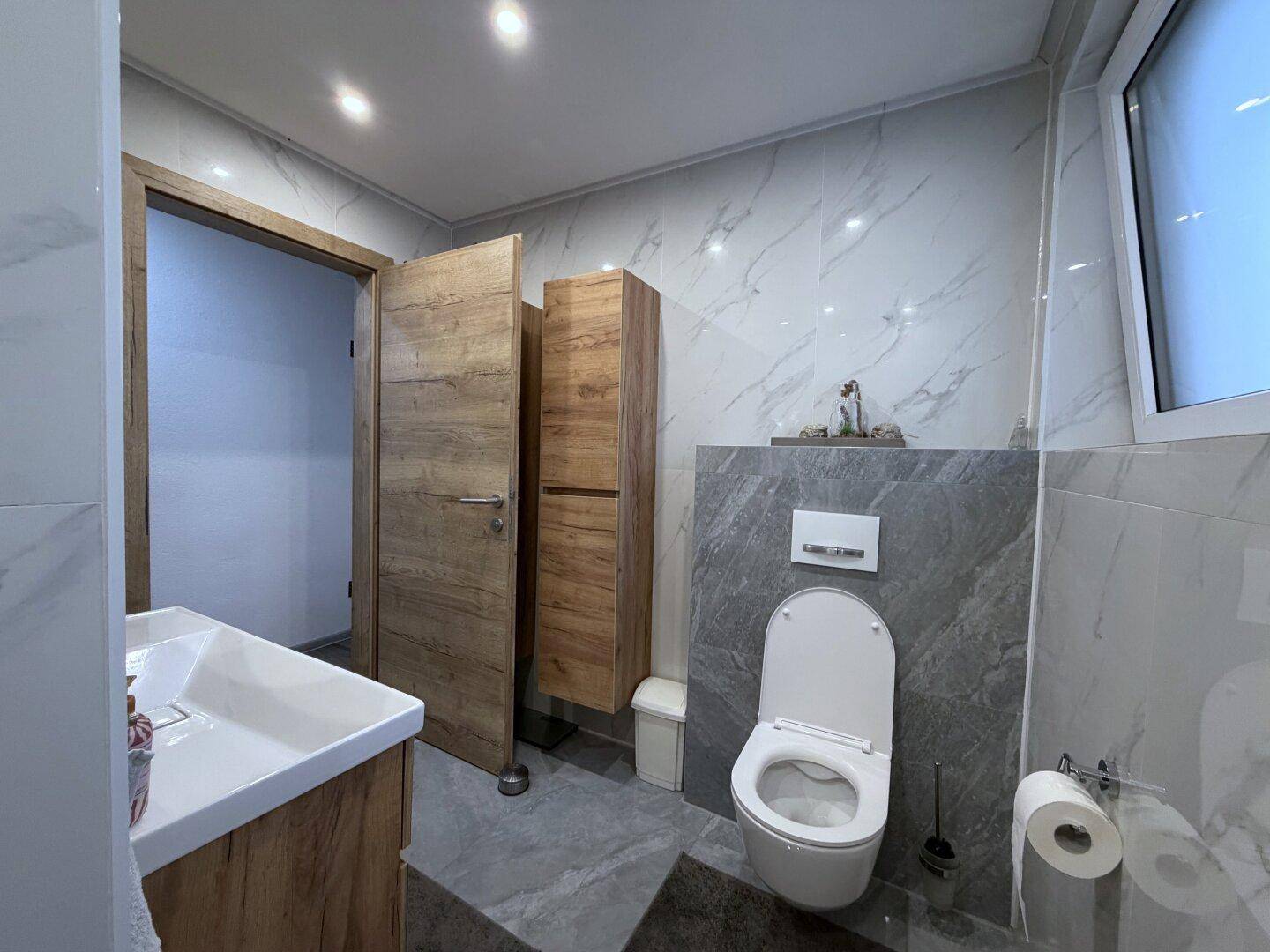 Helles Badezimmer mit Marmorfliesen, Waschtisch und wandhängendem WC.