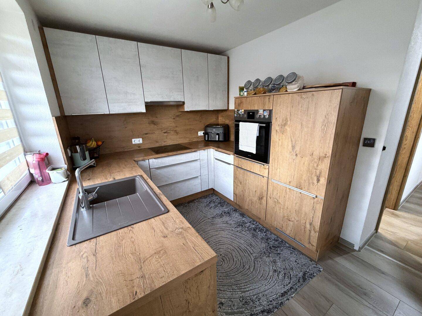 Moderne Küche mit Holz- und weißen Schränken, integriertem Backofen und Spüle.