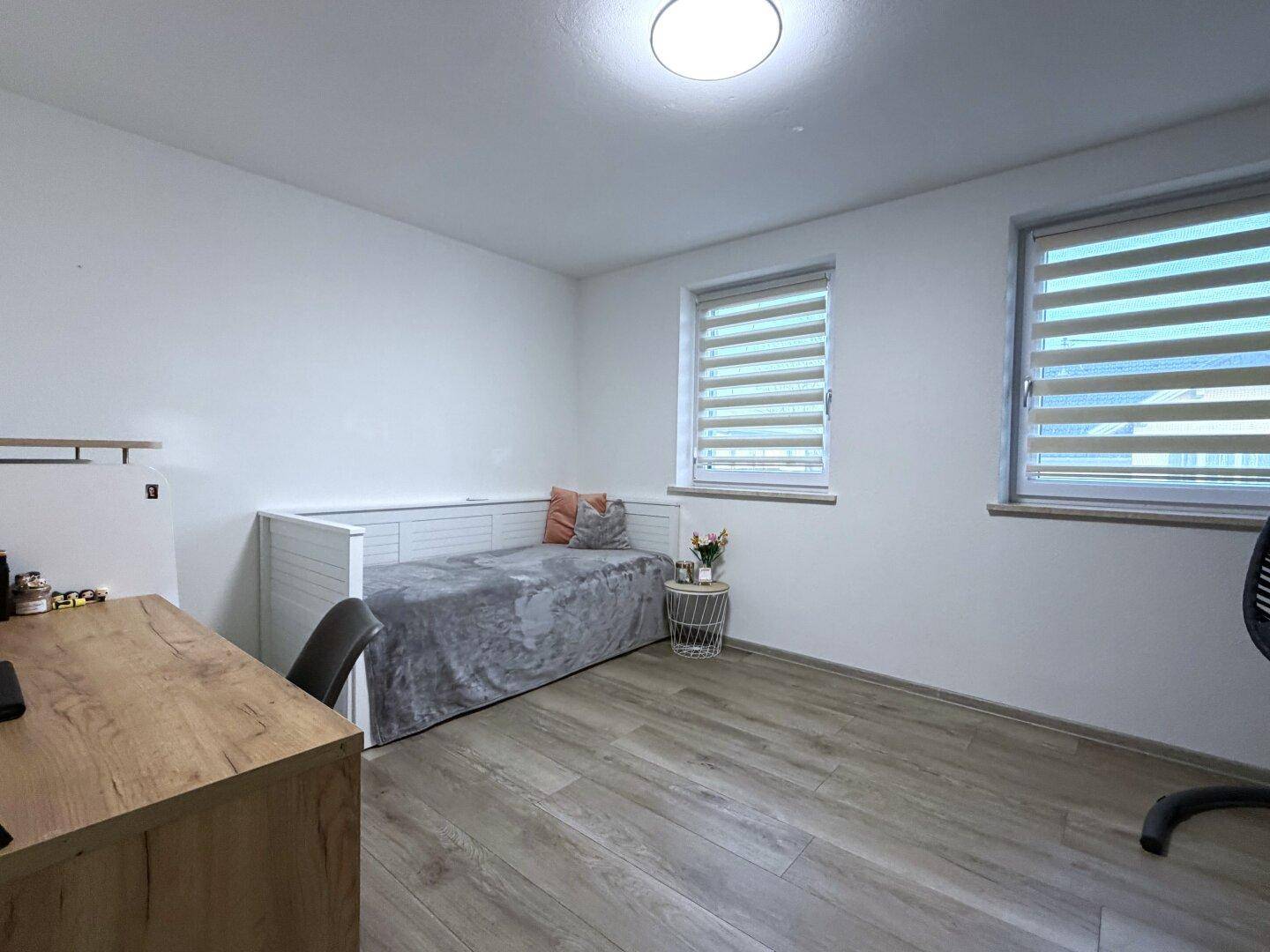 Helles Zimmer mit Holzboden, Tagesbett und zwei Fenstern für viel Tageslicht.