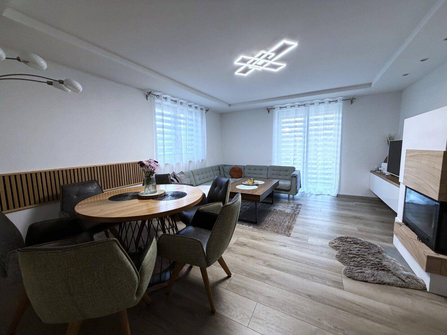 Moderner Wohn-Essbereich mit Holzboden, stilvoller Deckenbeleuchtung und großem Sofa.