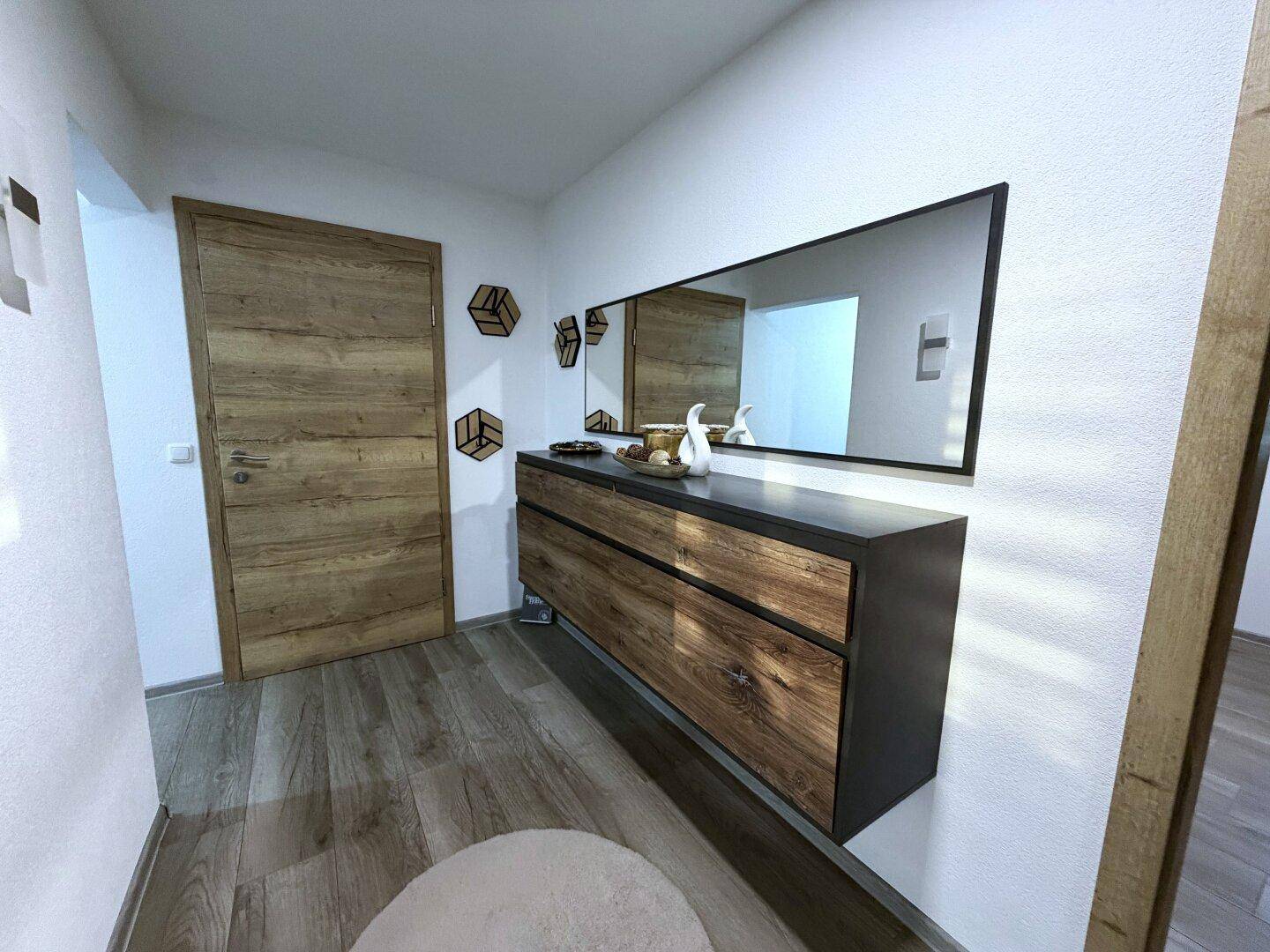 Eingangsbereich mit Holzboden, modernem Sideboard und großem Spiegel.