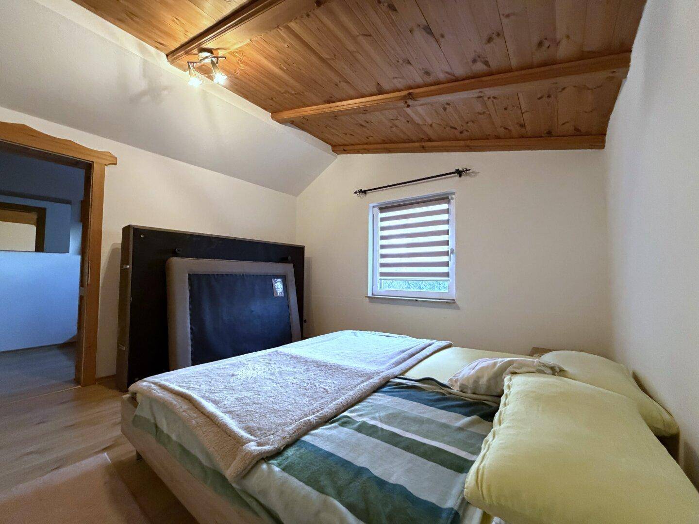 Gemütliches Schlafzimmer mit Holzboden, Doppelbett und Holzdecke.