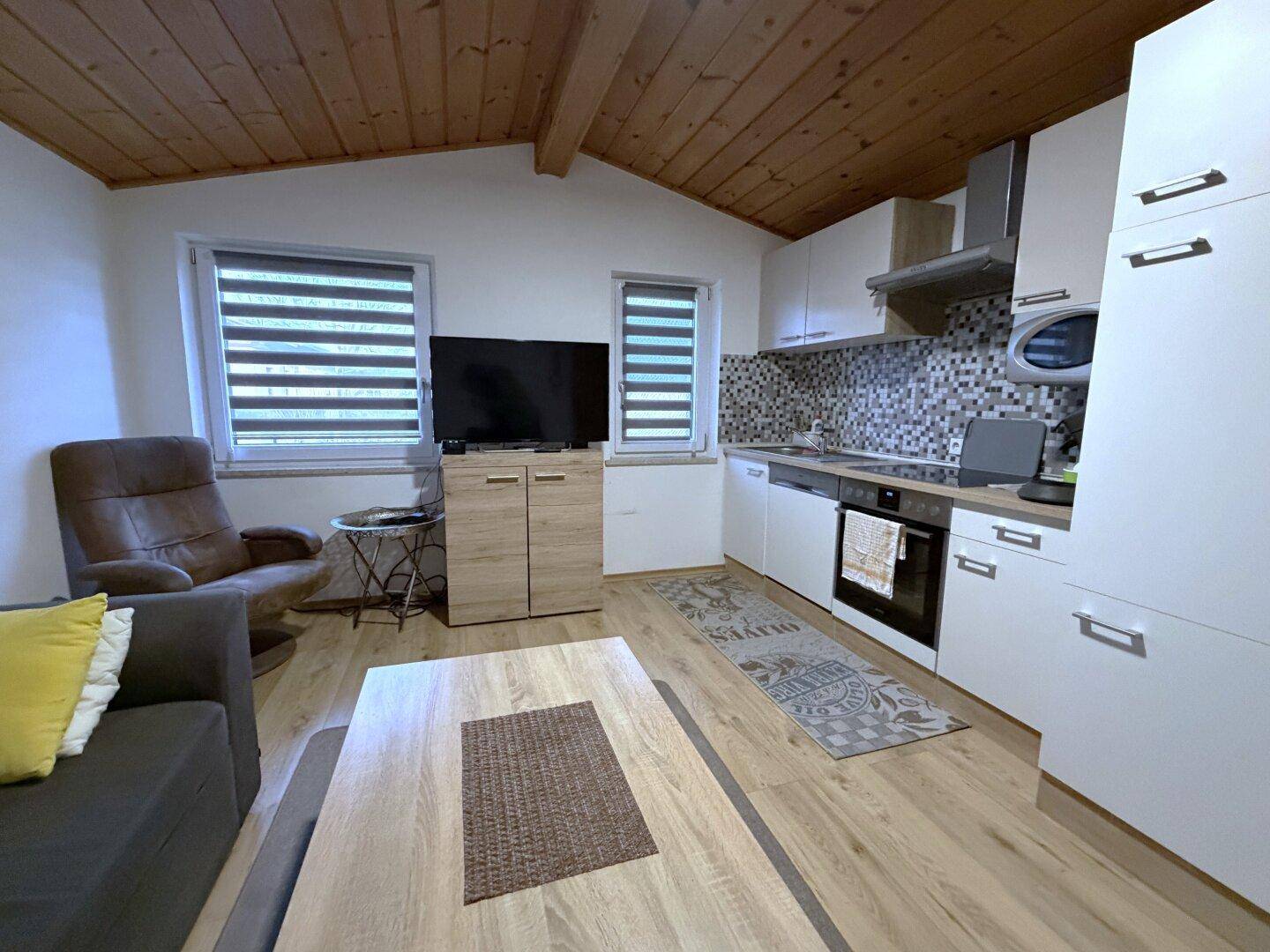 Offener Wohnbereich mit Küchenzeile, Holzboden und Holzdecke.