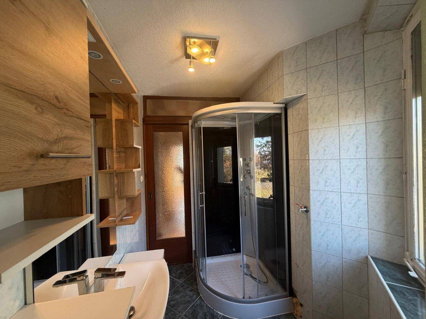 Badezimmer mit Duschkabine, Fliesenboden und Holzregalen für Stauraum.