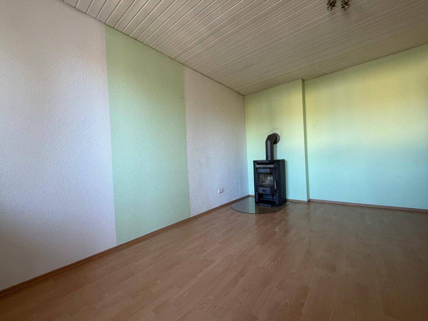 Gemütliches Wohnzimmer mit Holzboden, Kaminofen und hellgrünen Akzentwänden.