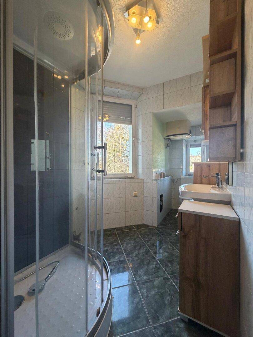 Badezimmer mit Duschkabine, Fenster und Fliesen an Wänden und Boden.