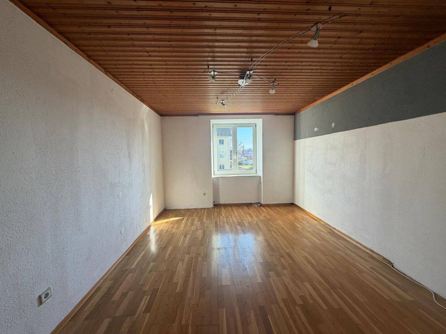 Helles Schlafzimmer mit Holzdeckenverkleidung, Laminatboden und großem Fenster.
