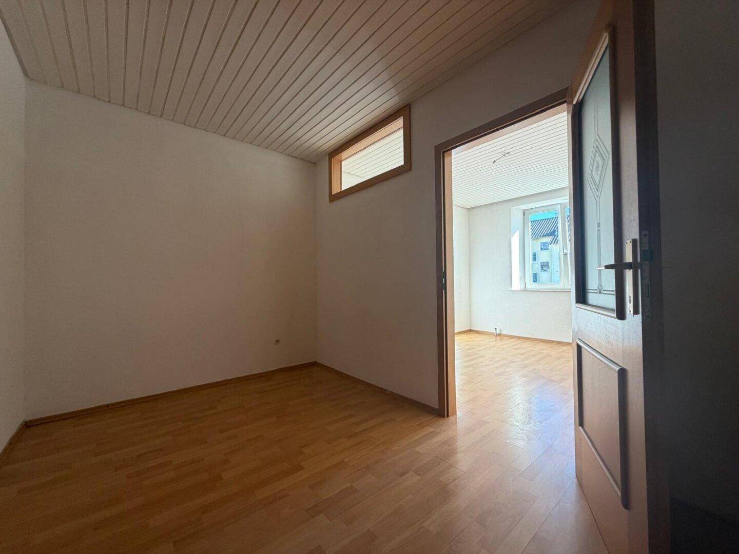 Leerer Raum mit Laminatboden und Holztür, der zu einem weiteren Zimmer führt.