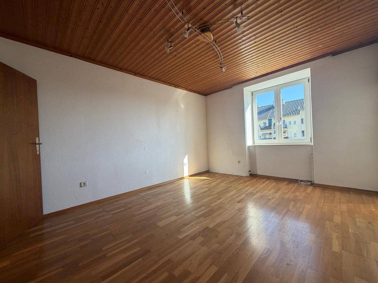 Geräumiges Schlafzimmer mit Holzdeckenverkleidung, Laminatboden und viel natürlichem Licht.