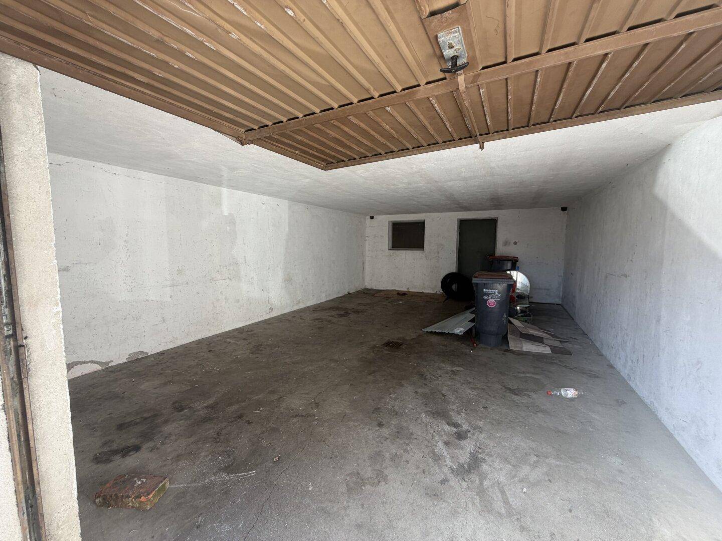 Geräumige Garage mit Betonboden und einfachem Garagentor, ideal für Fahrzeuge oder Lagerung.