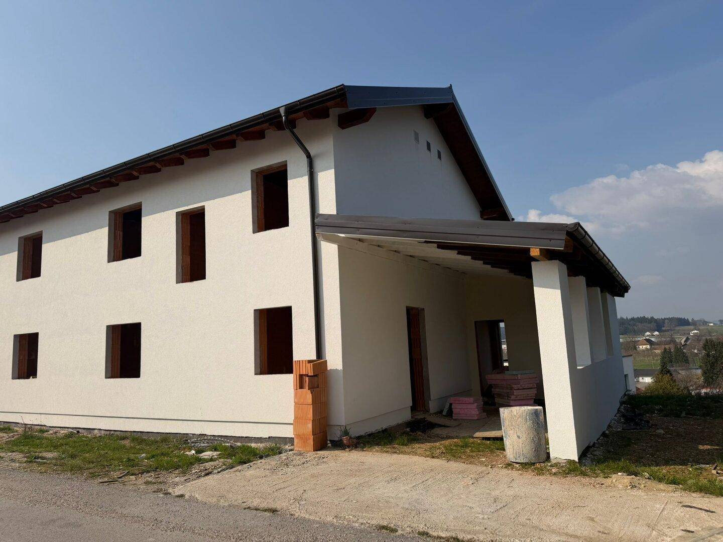 Seitenansicht des Neubaus mit weißer Fassade, Satteldach und einem überdachten Bereich.