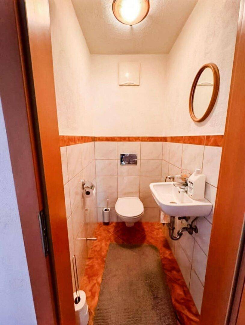 Gäste-WC mit Wand-WC, Waschbecken und Fliesen in Terrakotta-Optik.