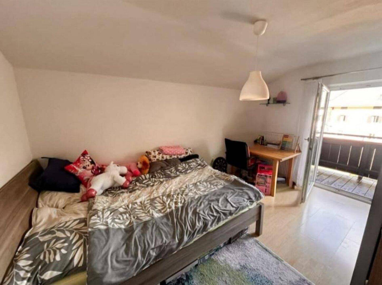 Kinderzimmer mit Bett, Schreibtisch und Zugang zu einem kleinen Balkon.