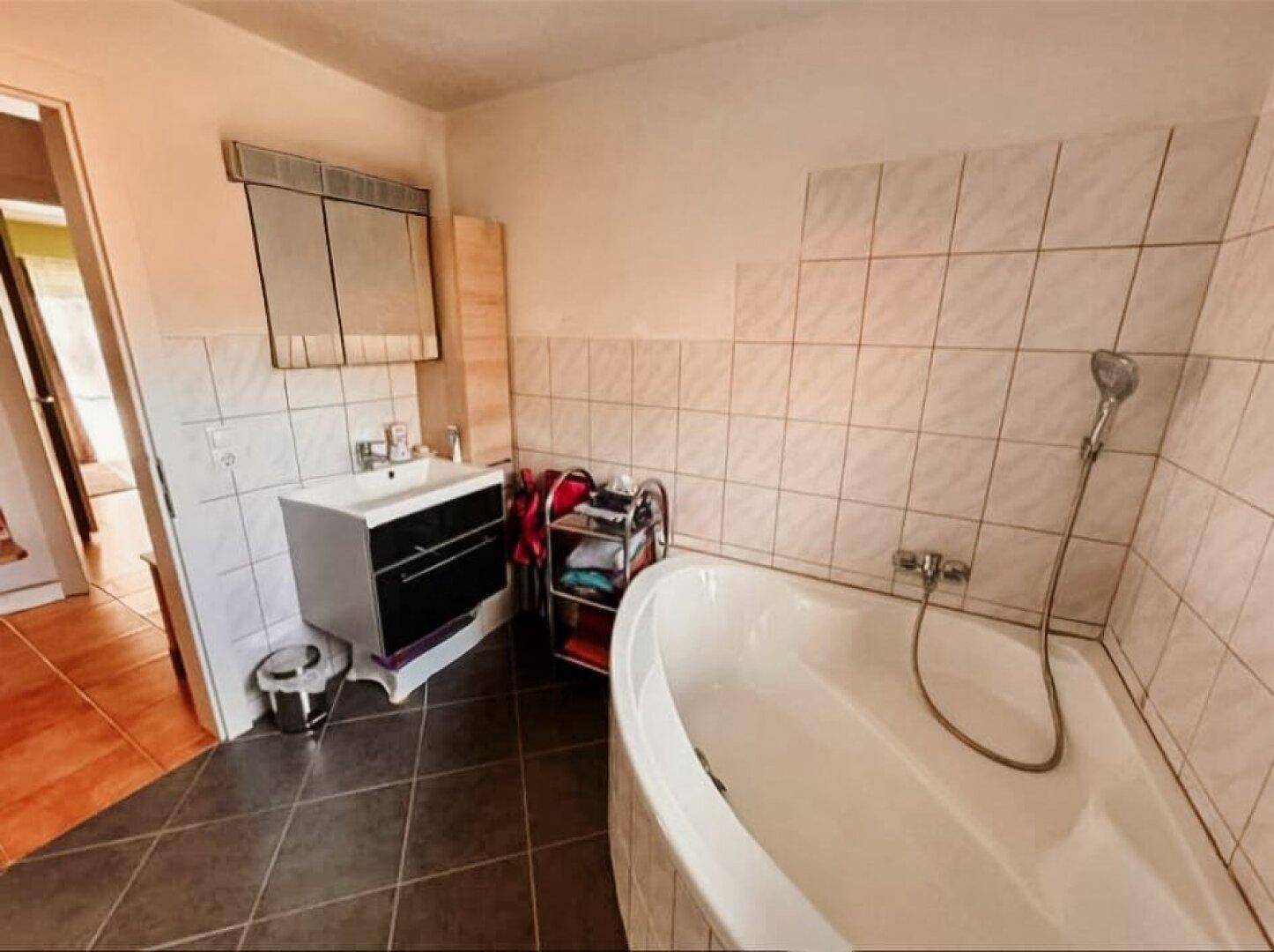 Badezimmer mit Badewanne, Waschbecken und dunklen Bodenfliesen.