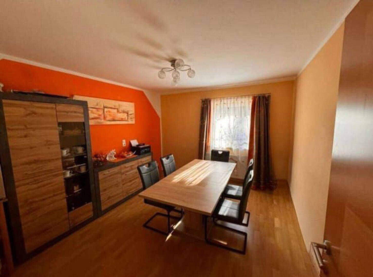 Esszimmer mit großem Holztisch, orangefarbenen Wänden und Holzschrank.