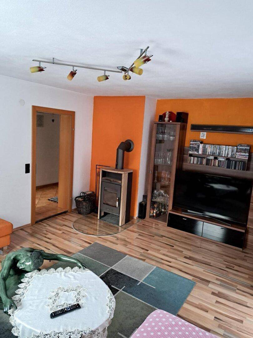 Wohnzimmer mit Holzboden, Kaminofen und orangefarbener Akzentwand.