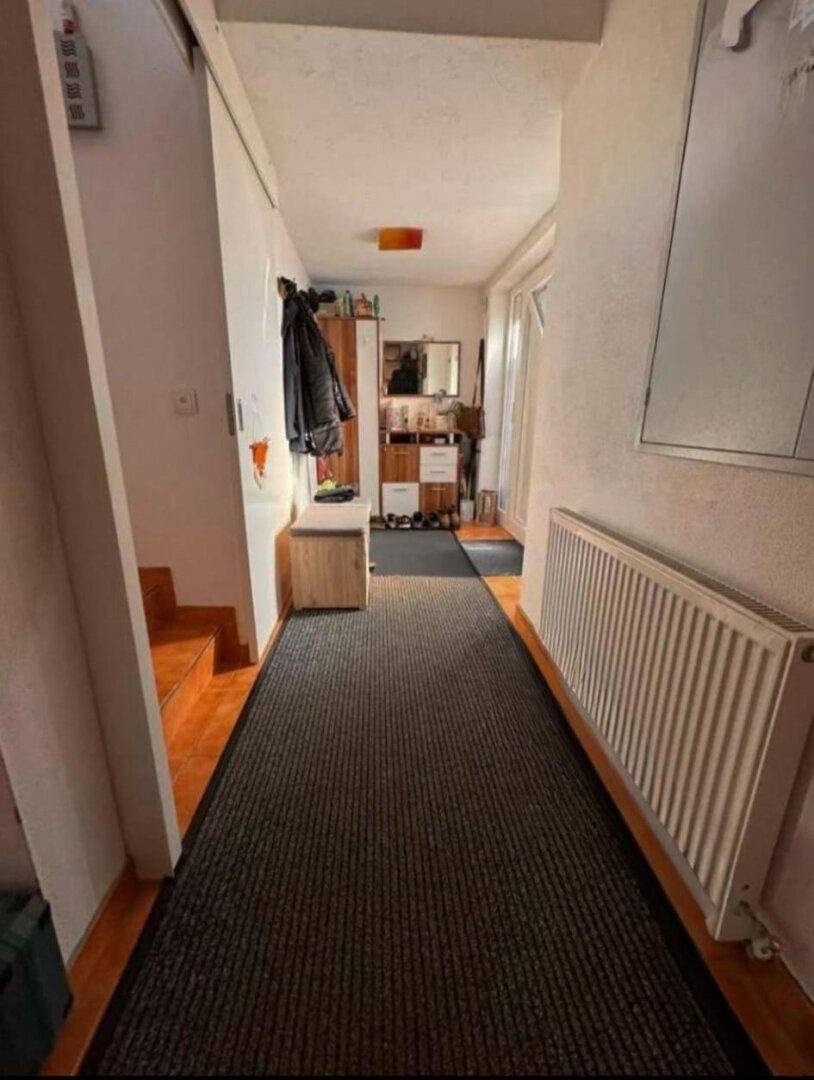 Langer Flur mit Garderobe, Heizkörper und Teppichläufer.