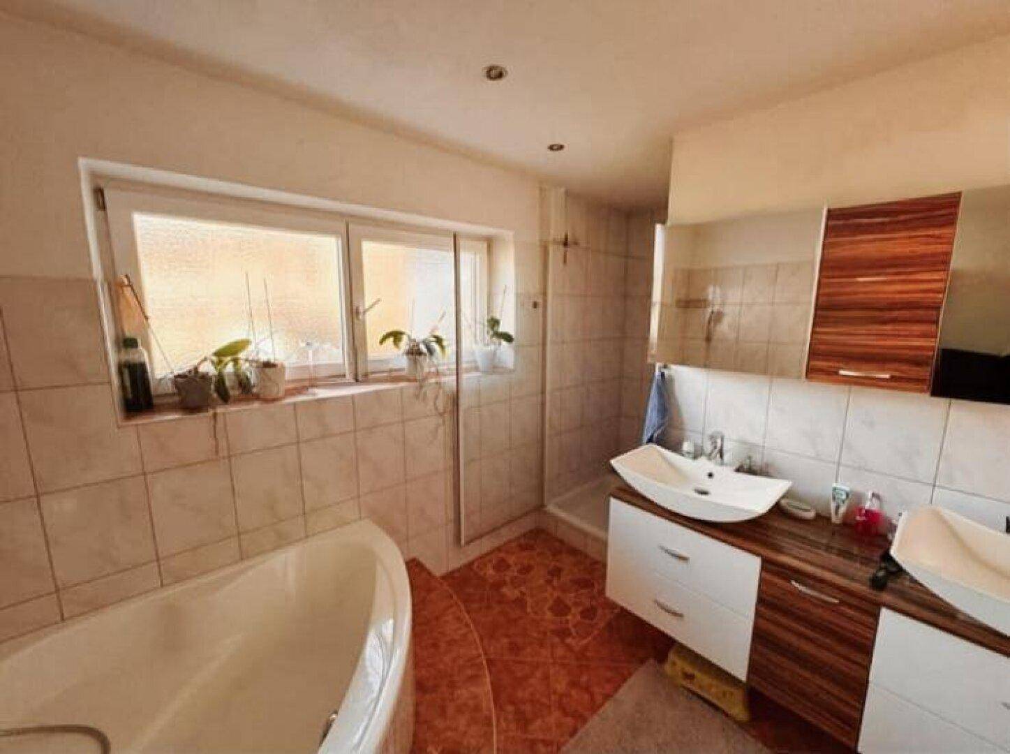 Badezimmer mit Eckbadewanne, Dusche und Doppelwaschbecken unter einem Fenster.