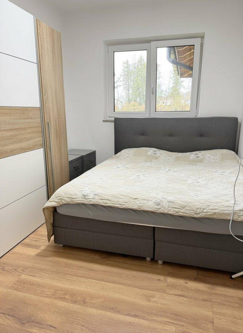 Helles Schlafzimmer mit Doppelbett, Kleiderschrank und Laminatboden.
