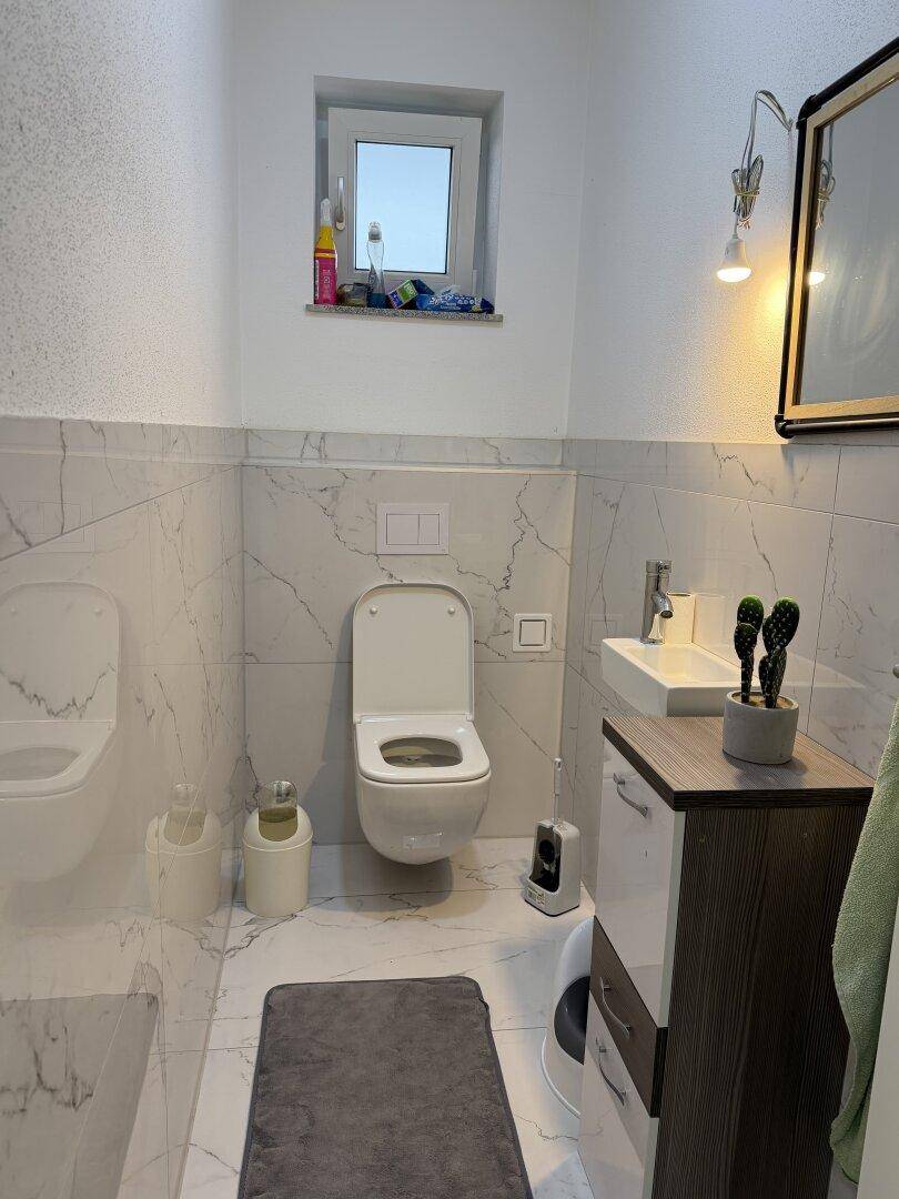 Modernes Gäste-WC mit wandhängendem WC, kleinem Waschbecken und Fenster.