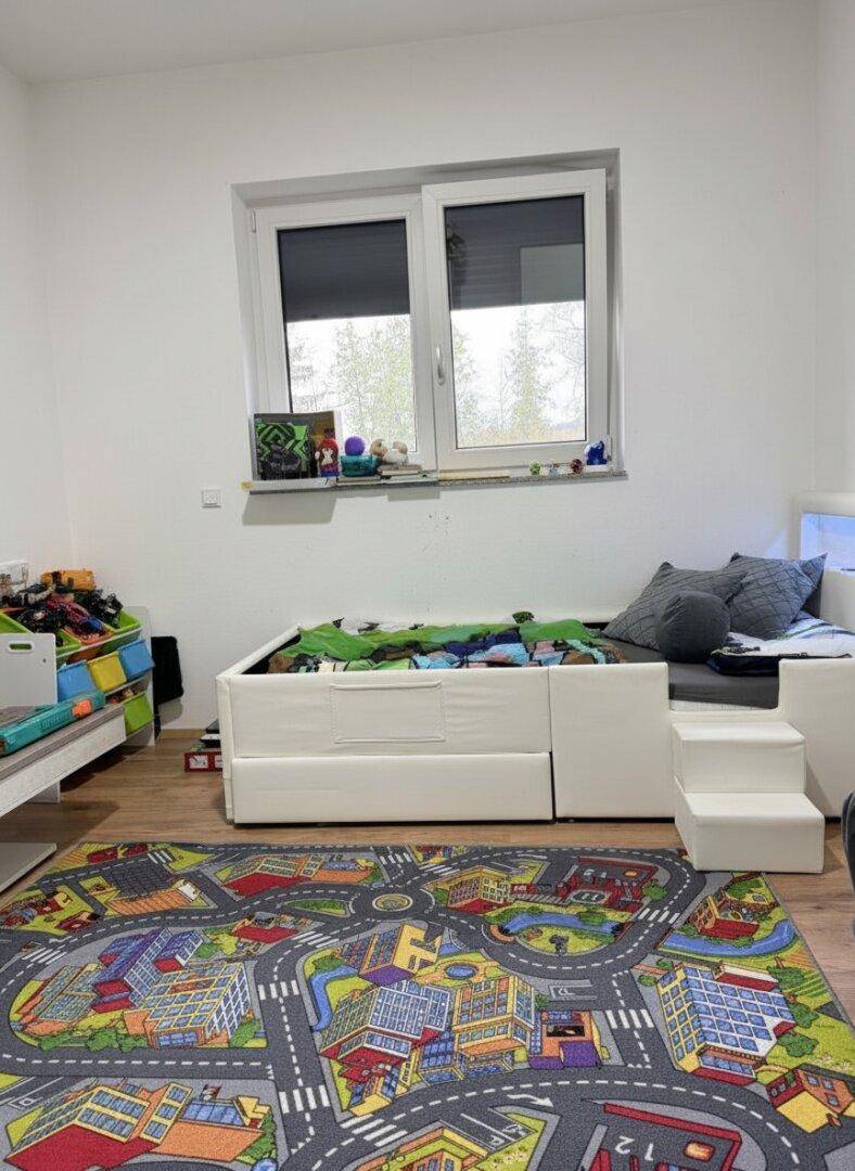 Kinderzimmer mit Spielteppich, Bett und Stauraum für Spielzeug, hell und freundlich gestaltet.
