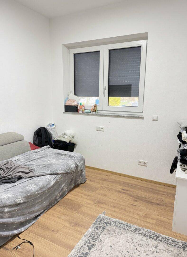 Einfaches Schlafzimmer mit Bett und Fenster, ausgestattet mit Laminatboden.