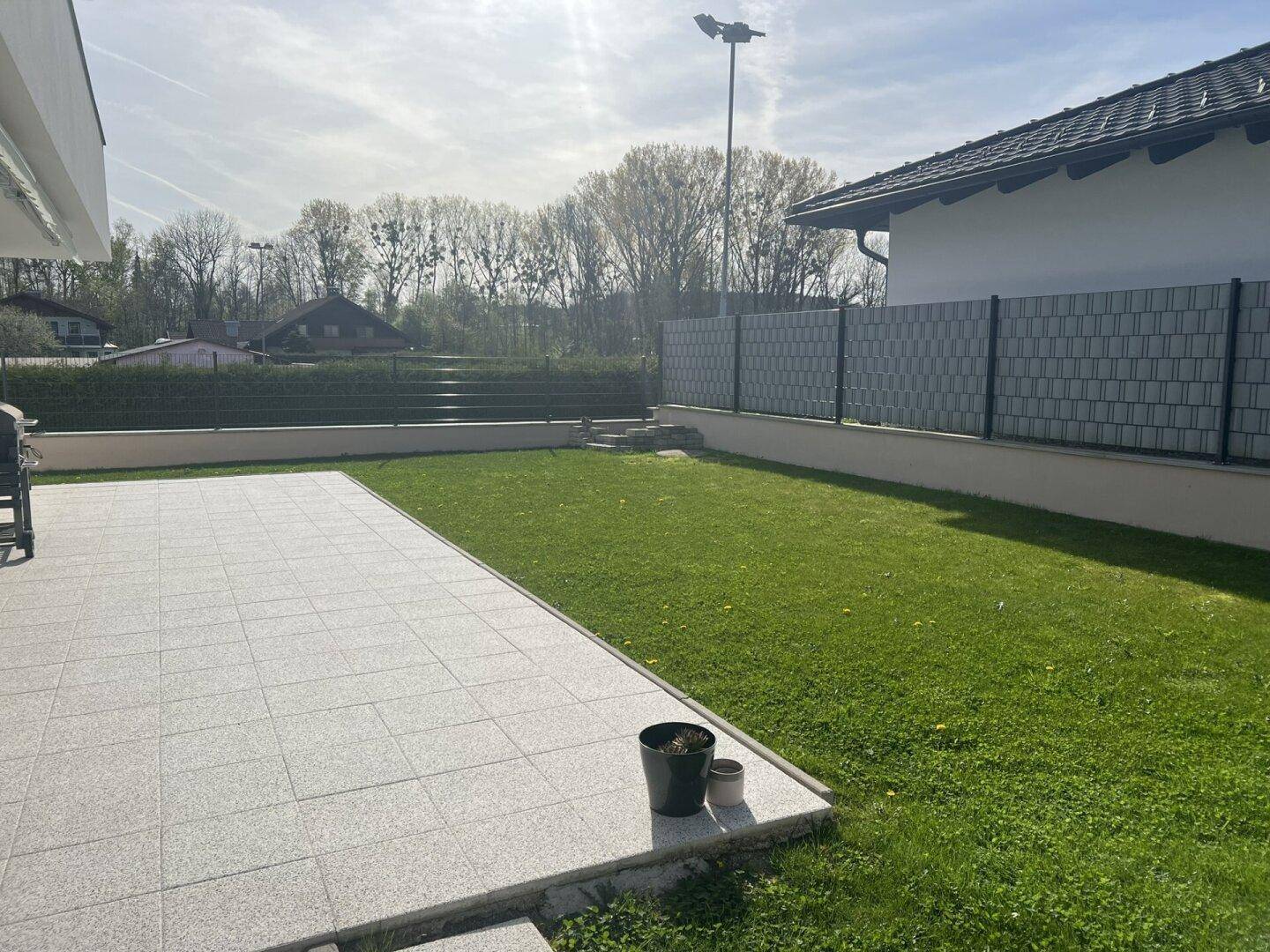 Gepflegter Garten mit Rasenfläche und großer gepflasterter Terrasse.