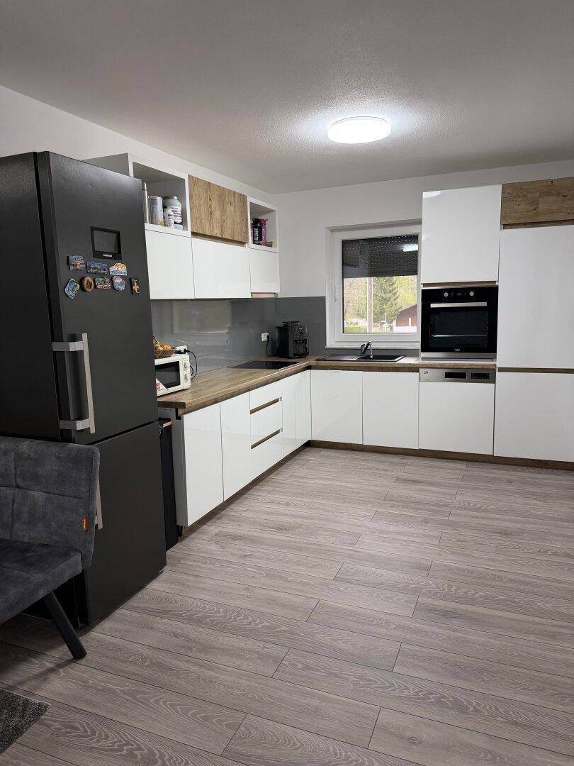 Moderne Küche mit weißen Hochglanzfronten, dunklem Kühlschrank und Holzboden.