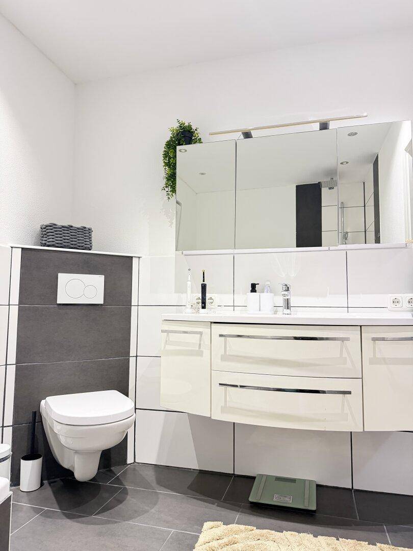 Modernes Badezimmer mit wandhängender Toilette, Waschtisch und Spiegelschrank.