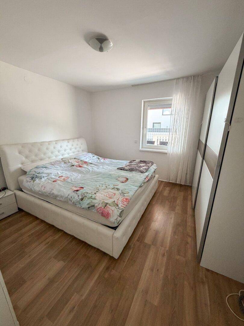 Schlafzimmer mit großem Doppelbett, Laminatboden und einem Fenster für natürliches Licht.