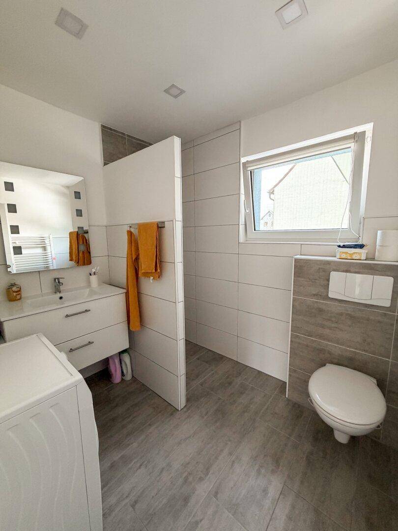 Modernes Badezimmer mit Dusche, WC, Einzelwaschbecken und einem Fenster für Belüftung.