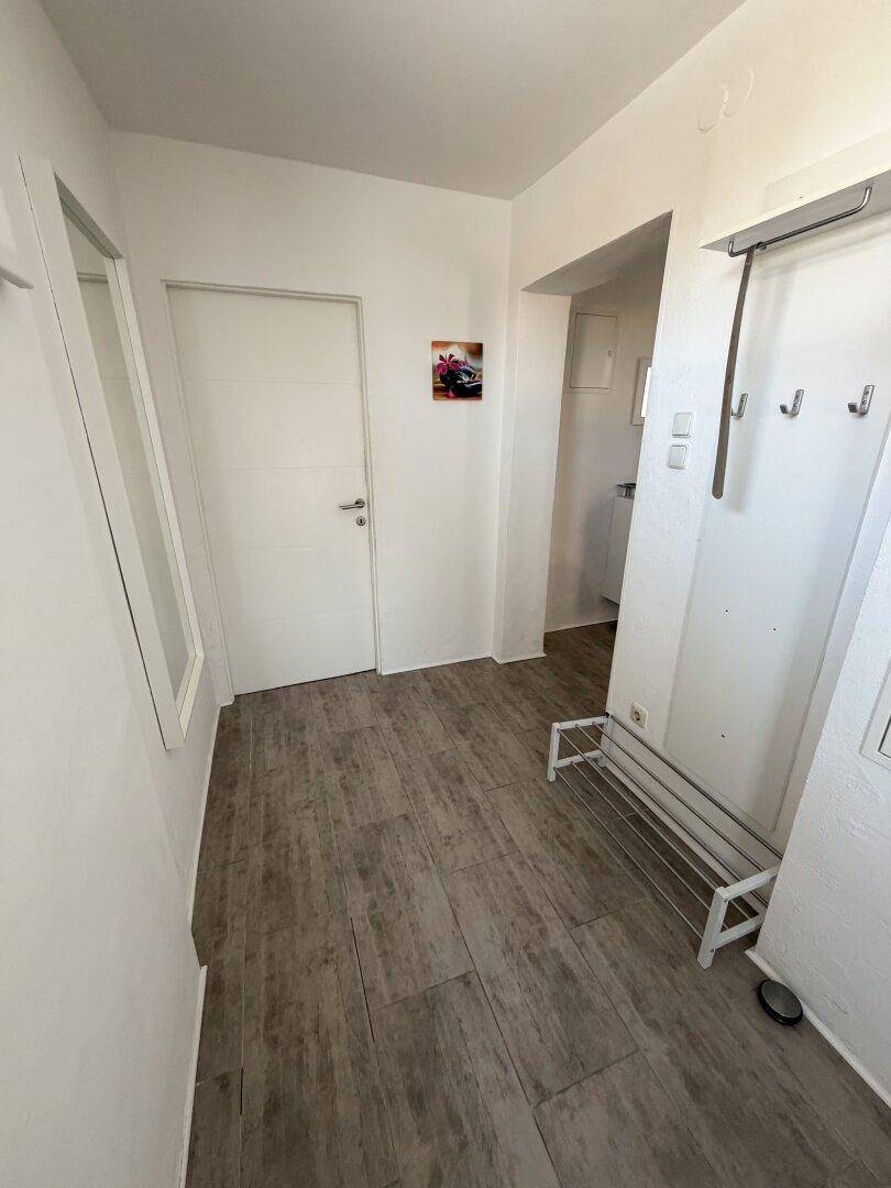 Eingangsbereich mit Holzoptik-Boden, einem Spiegel und Garderobenmöglichkeiten.