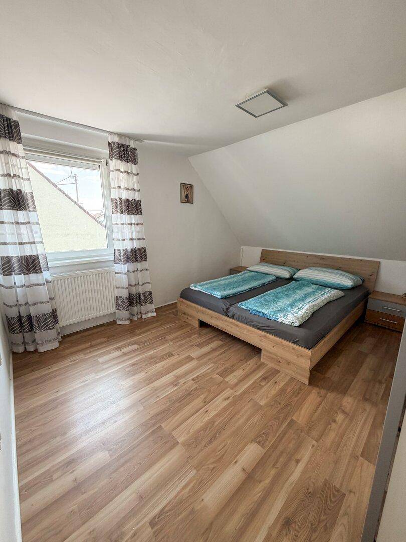 Dachgeschoss-Schlafzimmer mit Holzbett, Laminatboden und einem Fenster mit Ausblick.