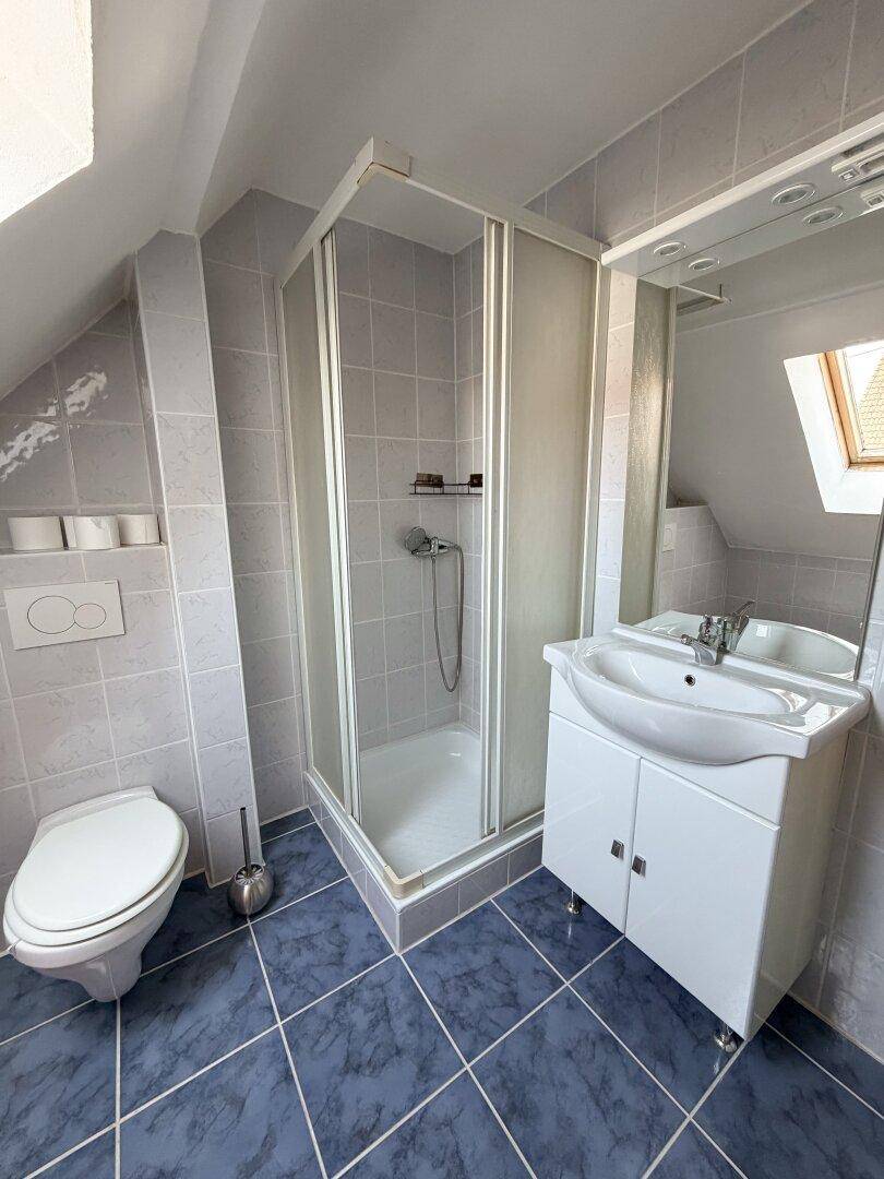 Dachgeschoss-Badezimmer mit Dusche, WC, Waschbecken und einem praktischen Dachfenster.