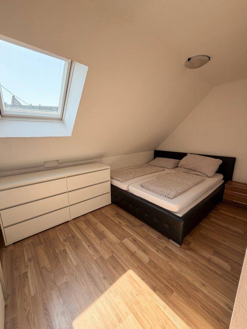 Weiteres Dachgeschoss-Schlafzimmer mit Bett, Kommode und einem Dachfenster.