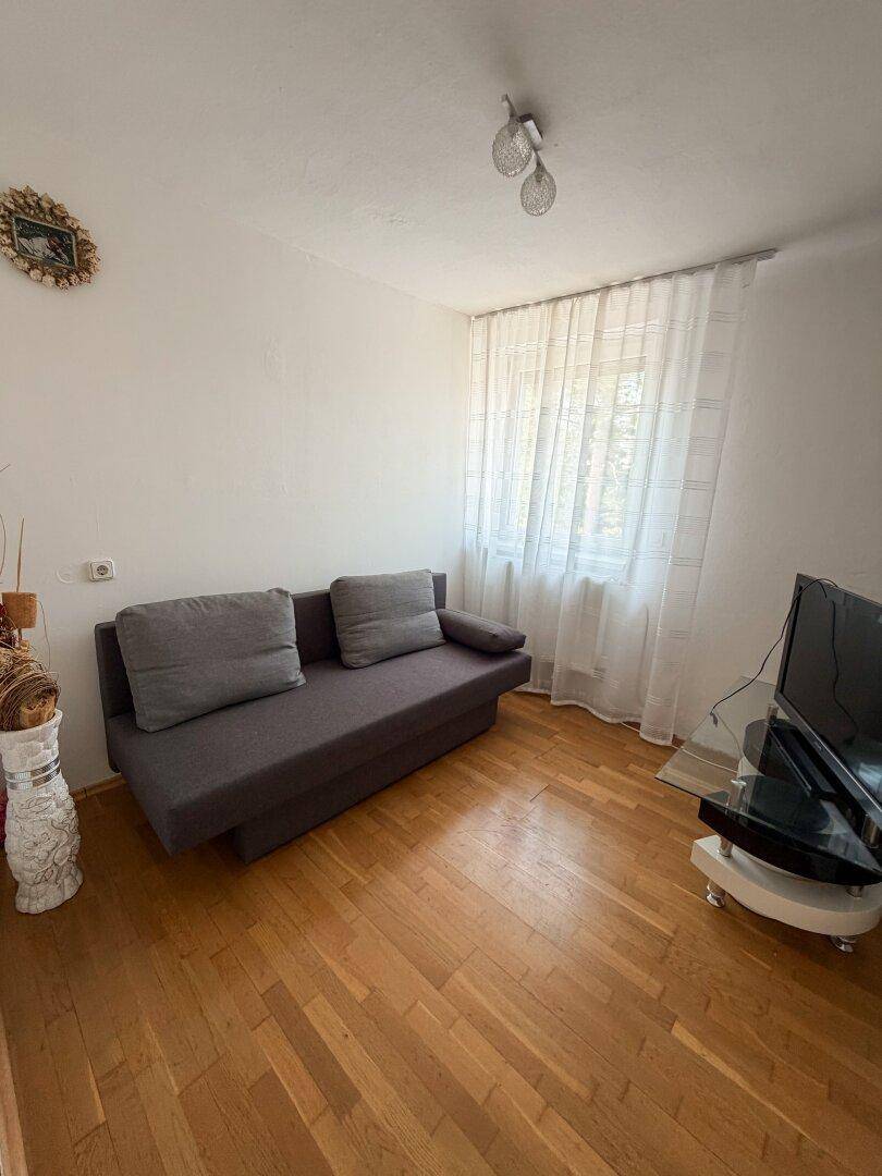 Gemütliches Zimmer mit Sofa, Holzboden und einem Fenster mit Vorhängen.
