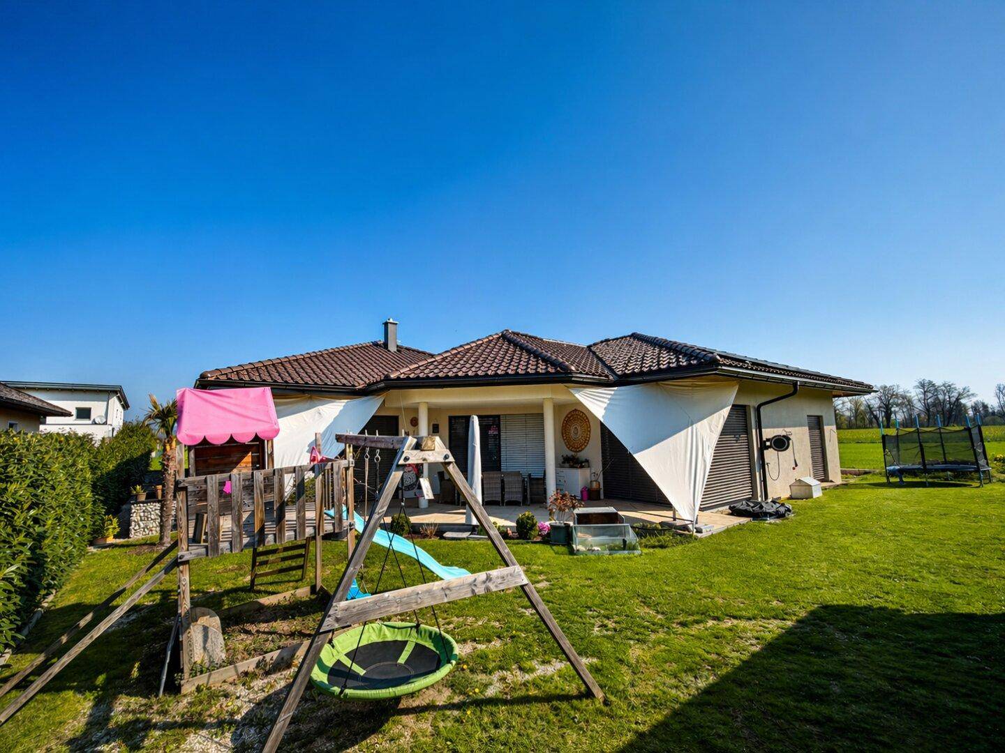 Großer Garten mit Spielplatz, Rasenfläche und überdachter Terrasse.