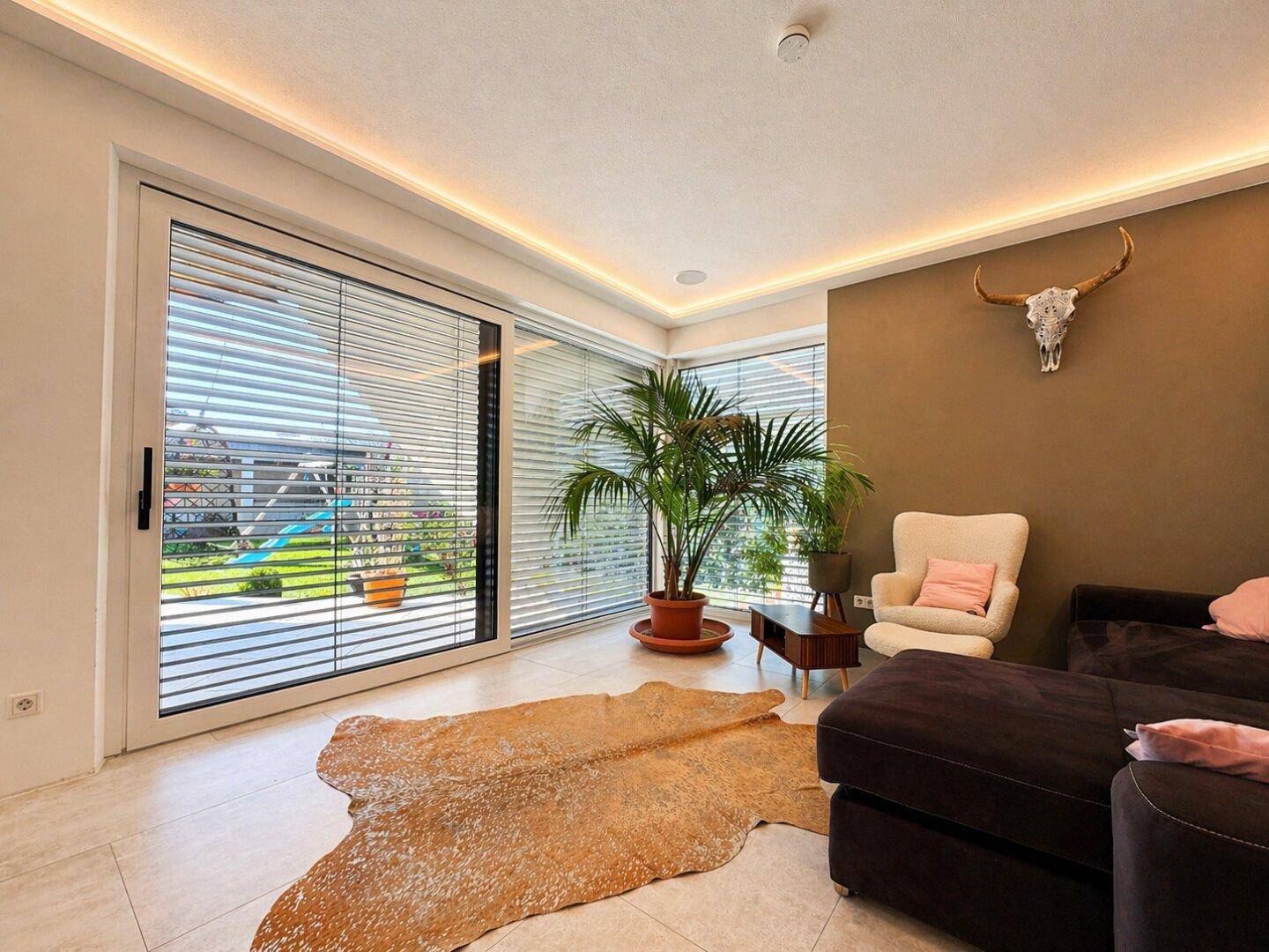 Helles Wohnzimmer mit großzügigen Fenstern, Blick in den Garten und Fliesenboden.