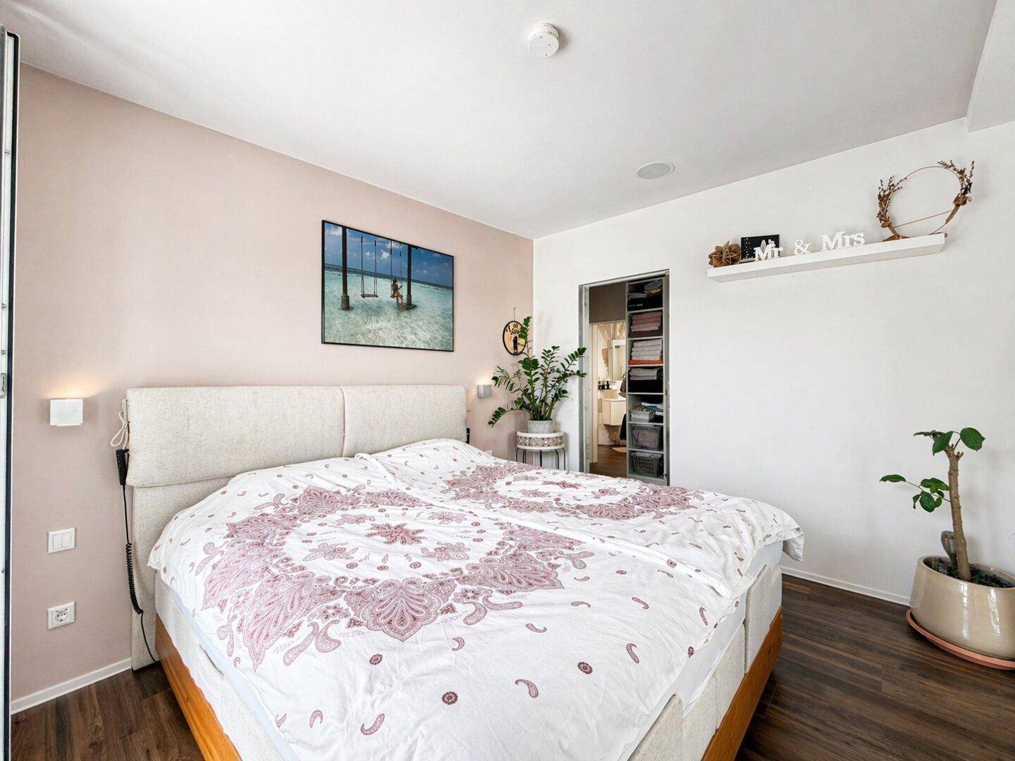 Helles Schlafzimmer mit Doppelbett, rosa Akzentwand und Zugang zum begehbaren Kleiderschrank.