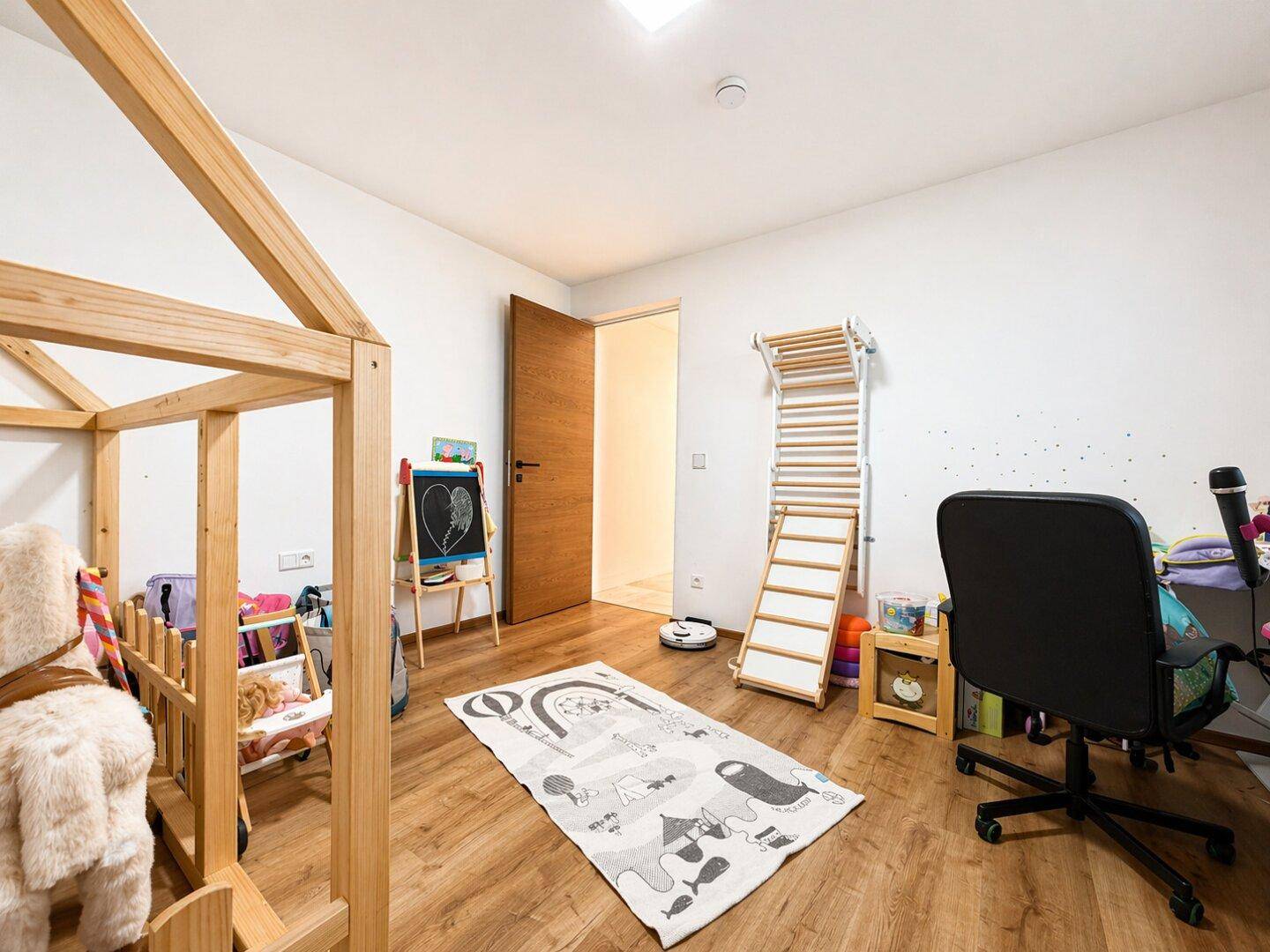 Geräumiges Kinderzimmer mit Spielgeräten, Schreibtisch und Holzboden.