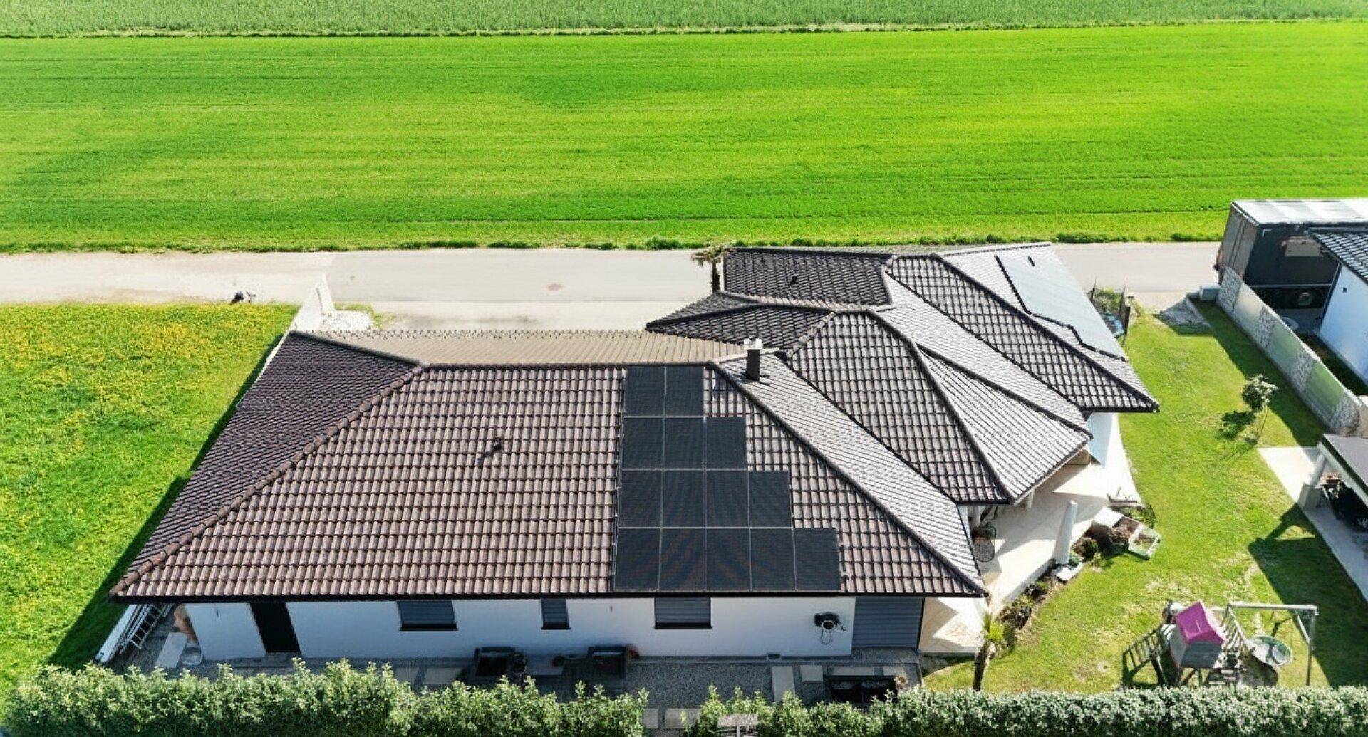 Luftaufnahme eines Einfamilienhauses mit Photovoltaikanlage auf dem Dach und grüner Umgebung.