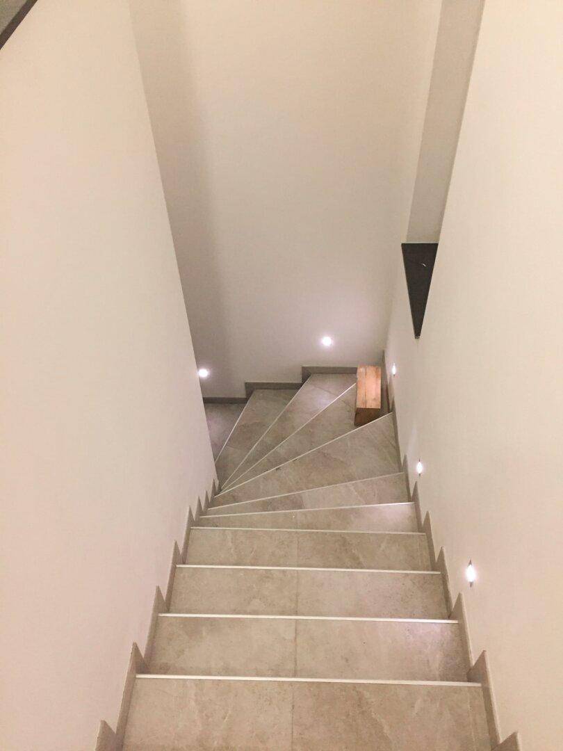 Moderne Treppe mit Fliesenstufen und integrierter Wandbeleuchtung für sicheren Aufstieg.
