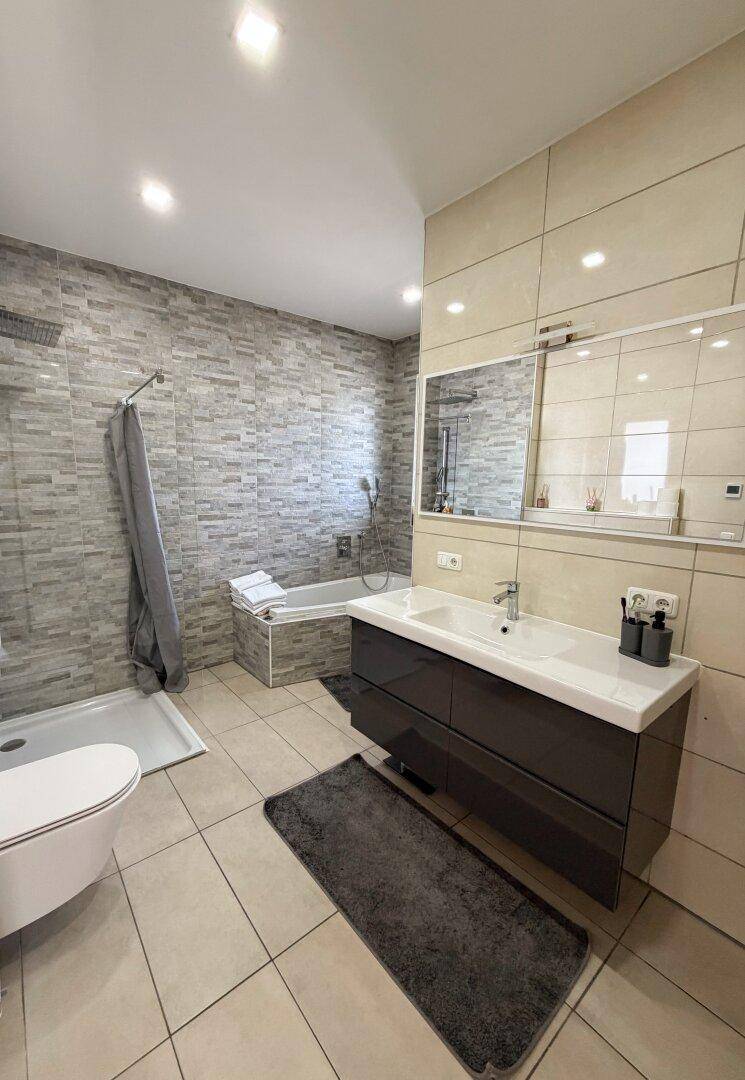 Modernes Badezimmer mit Badewanne, Dusche, Einzelwaschbecken und hellen Fliesen.